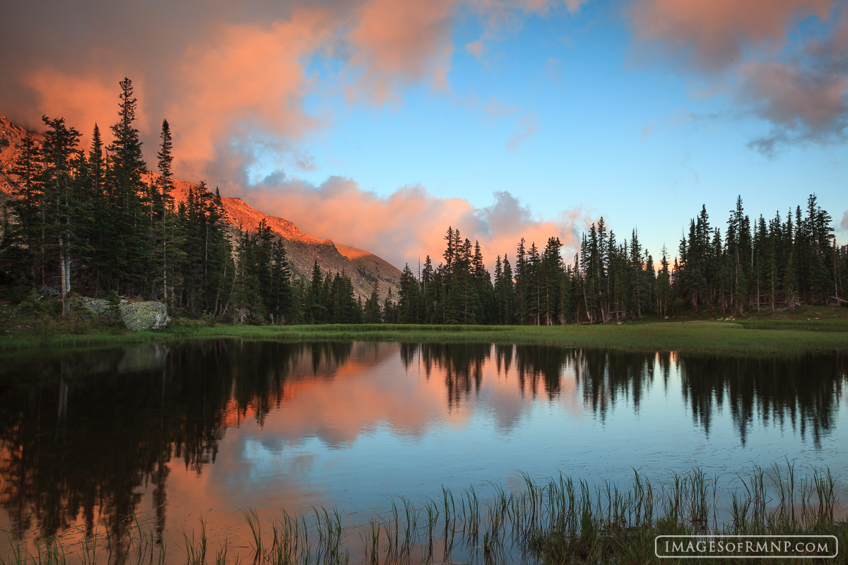 A small tarn in Rocky Mountain National Park reflects the brilliant sky while clouds above frame the colorful and tranquil scene...