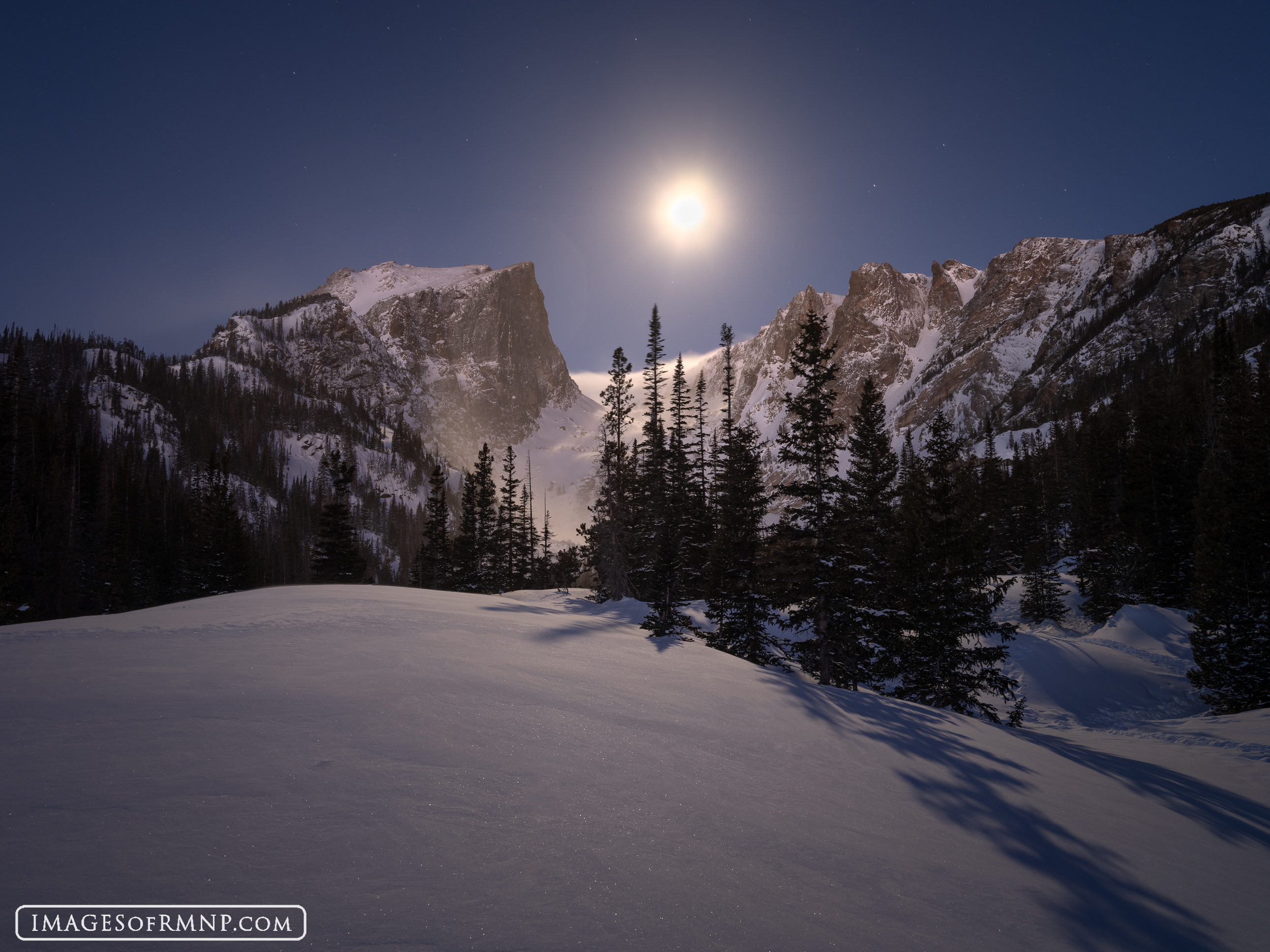 Hallett Peak and Flattop Mountain are gently warmed by the predawn light from the east. At the same time a full moon sets between...