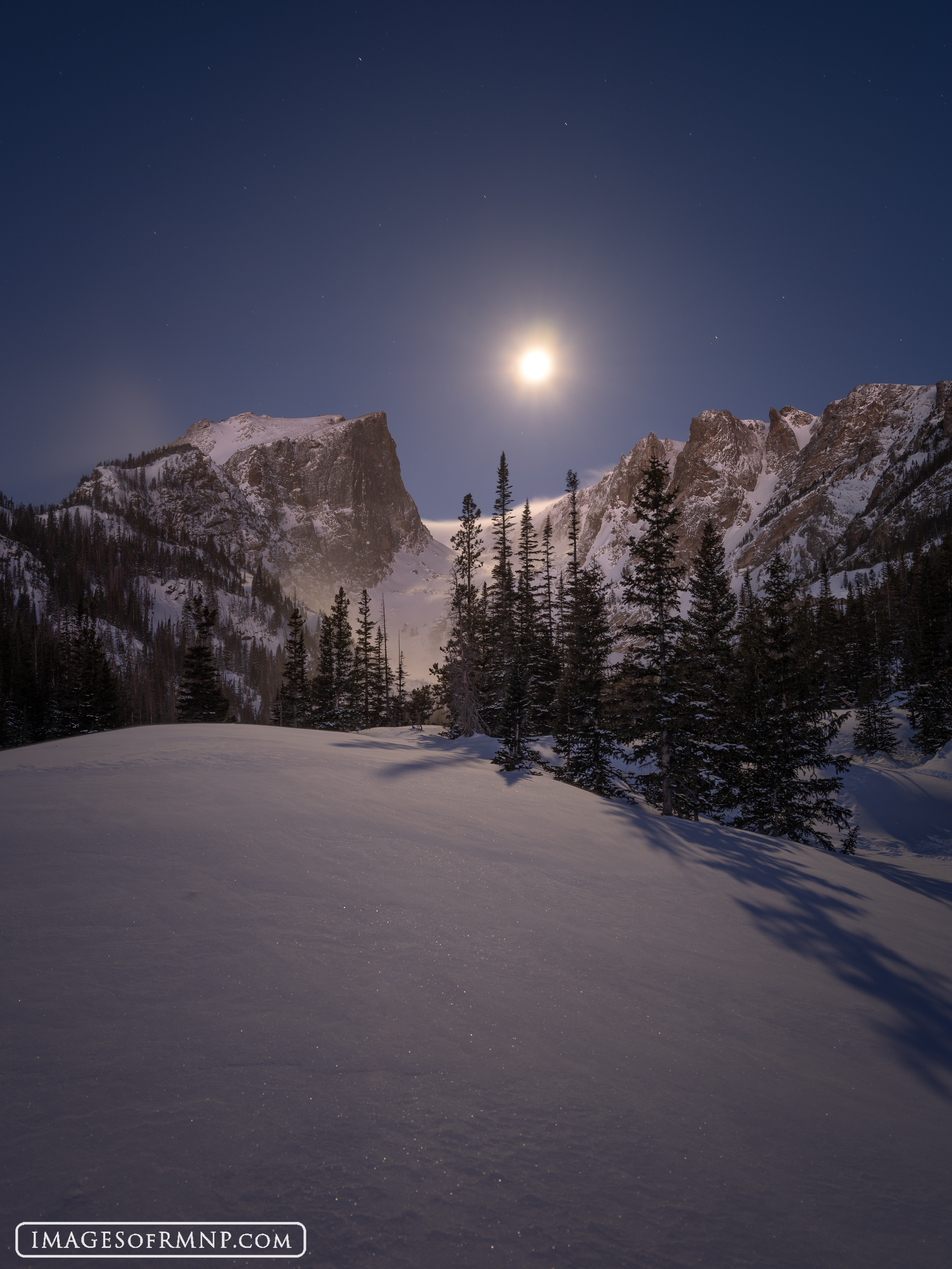 Hallett Peak and Flattop Mountain are gently warmed by the predawn light from the east. At the same time a full moon sets between...