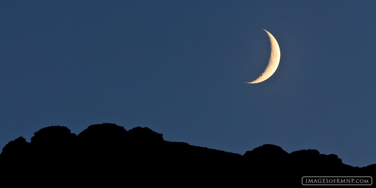 A crescent moon sets over Otis Peak in Rocky Mountain National Park