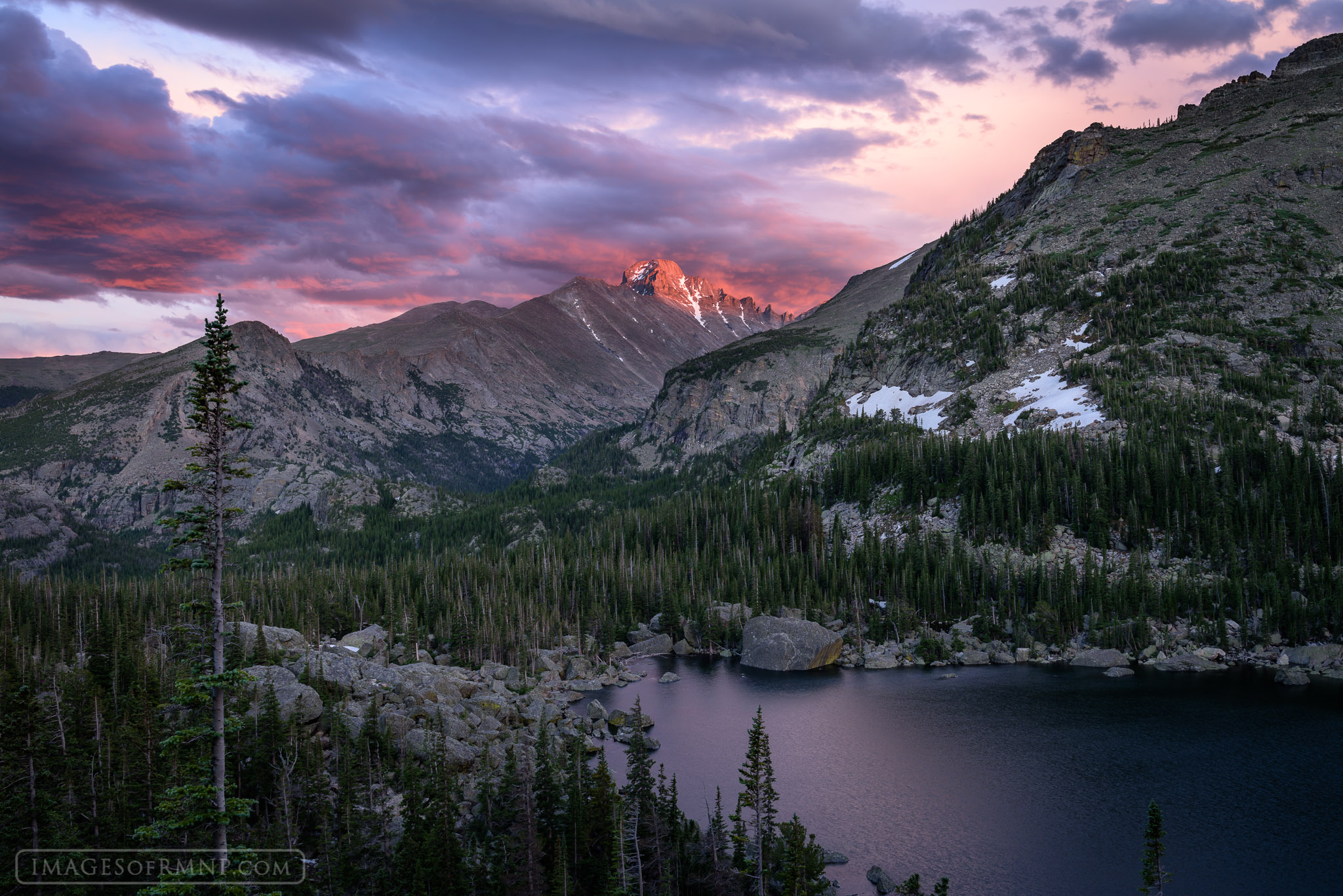Longs Peak towers over Lake Haiyaha on a beautiful summer evening as the clouds of a breaking storm glow in the light of a distant...