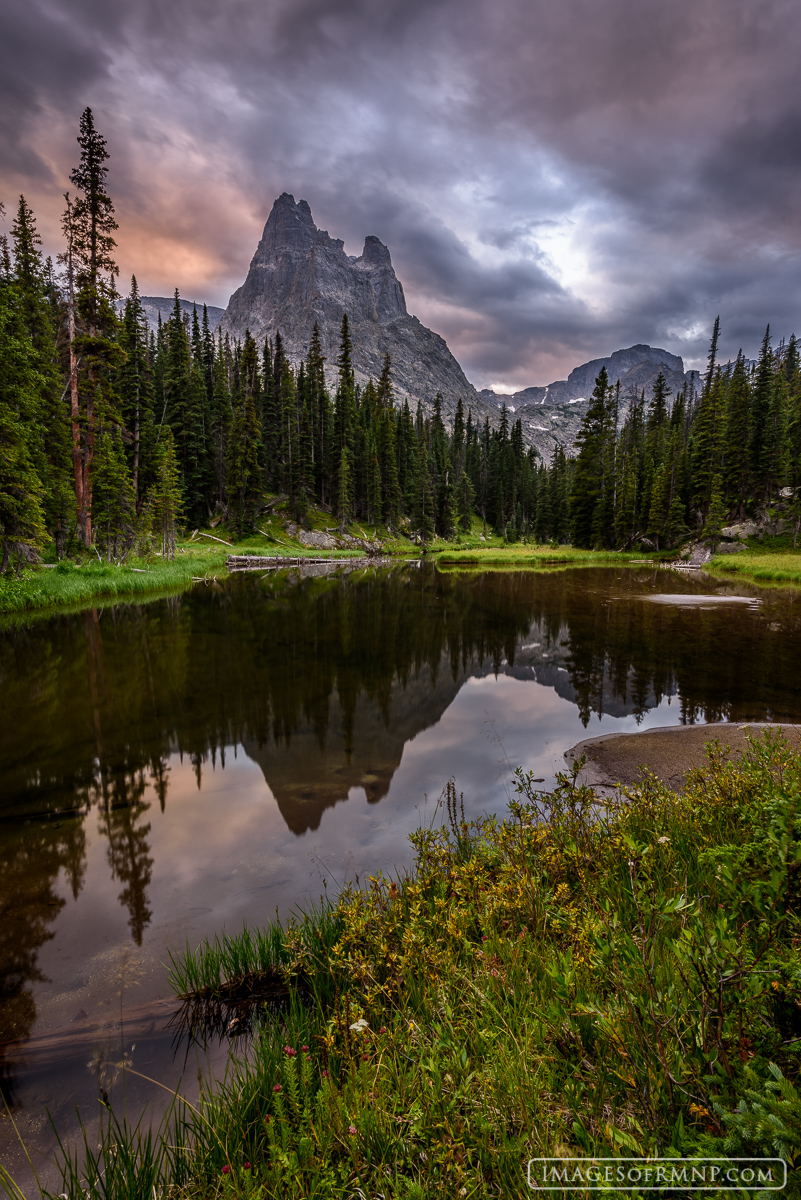 On a stormy evening far in the backcountry of Rocky Mountain National Park the jagged granite spires of a lone mountain reflect...