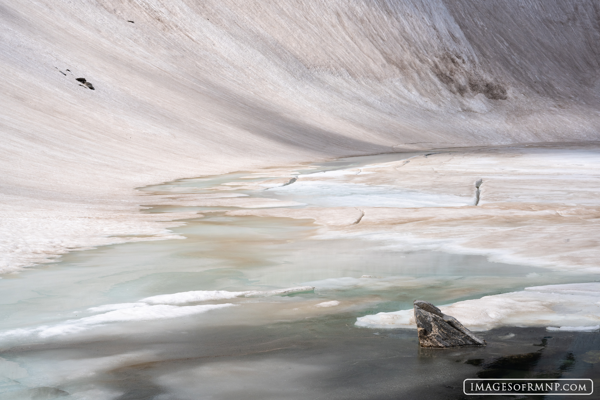 A high alpine lake surrounded by a wall of deep snow begins to thaw in early July. At well over 12,000' in elevation these lakes...