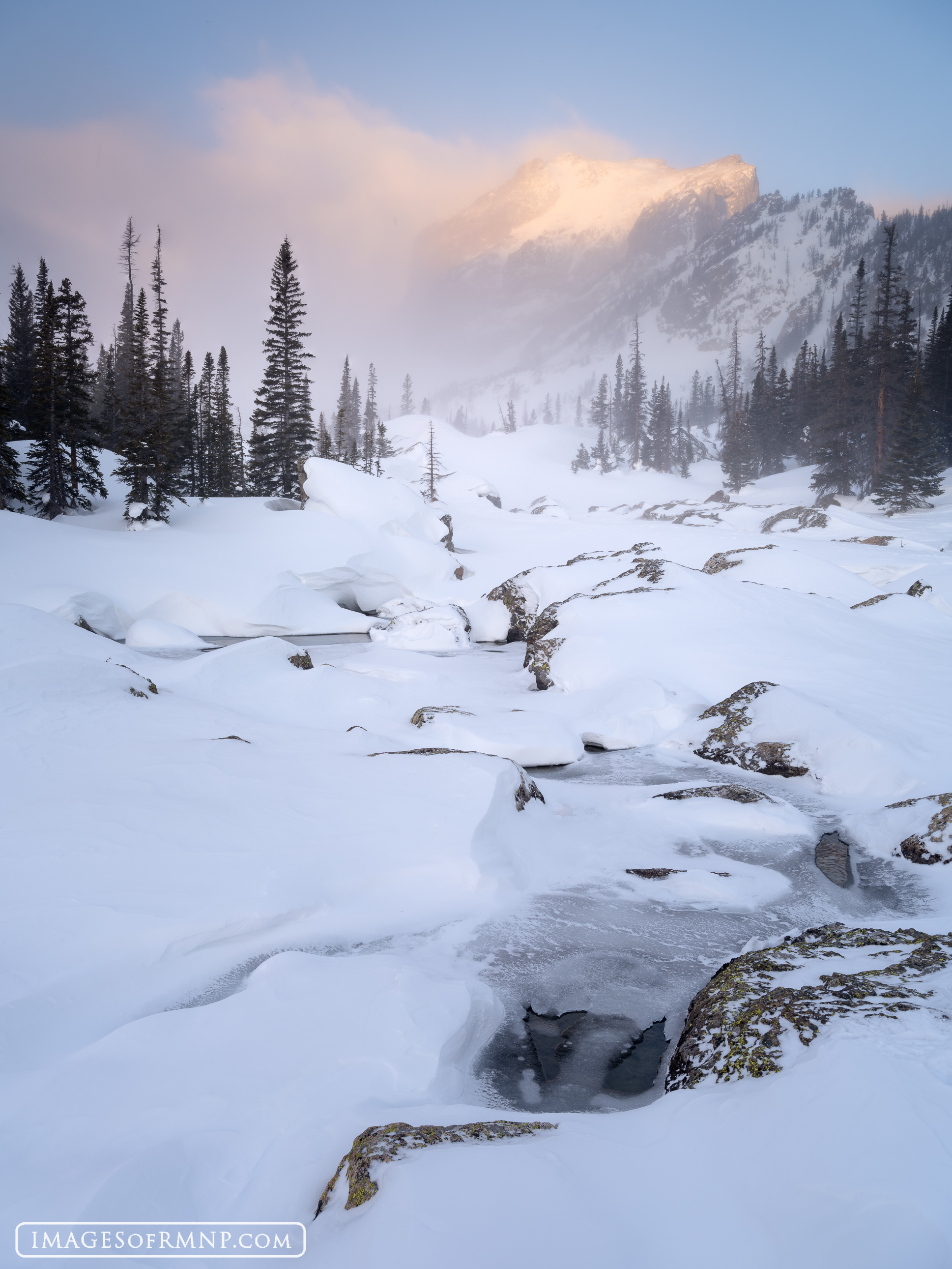 A partially frozen stream can be seen in this snowy landscape as Hallett Peak glows in the warm light on this chilly morning.