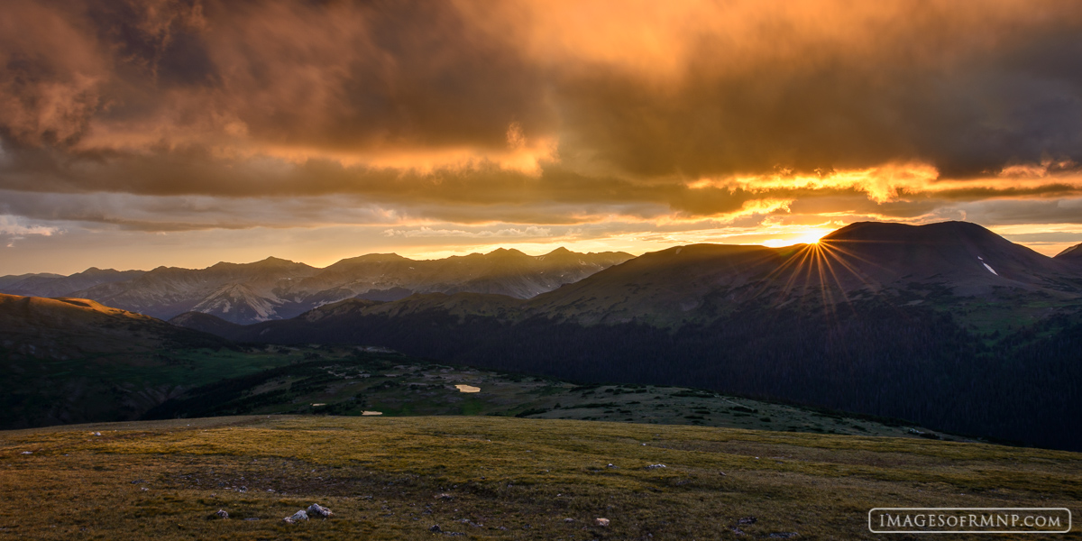 Warm light floods the sky as the sun sets behind Specimen Mountain in Rocky Mountain National Park as seen from the tundra near...